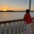 A person is standing by a decorative railing, observing the sunset over a tranquil body of water.