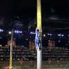 A performer is climbing a tall pole in front of an audience while others watch from the ground during what seems to be a lumberjack show or similar event.