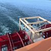 The image shows the red paddle wheels of a riverboat churning water, with a wooden frame structure in the foreground, possibly part of the boat's deck or a construction on it.