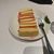 A slice of cheesecake with a strawberry drizzle is placed on a white plate beside a fork, ready to be enjoyed.