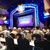 An audience is seated at tables in a theater, waiting for the performance of a show titled 