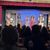 An audience watches performers on stage engaged in a scene from a play, which appears to have a rustic or western theme.