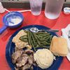 The image shows a meal consisting of green beans, mashed potatoes, shredded meat, a bread roll, and a small bowl of gravy, accompanied by two glasses of water on a red table.