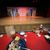 The image shows a partially eaten meal on a table with a clear view of a theater stage set with rustic barn doors in the background.