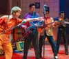 The image shows a lively scene with performers dressed in 1950s attire playing guitars and a double bass on stage while a person wearing vibrant clothing is upside down with legs in the air in front and theres a superimposed picture of a plate of food featuring what appears to be meat vegetables and bread