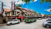 A quaint street scene featuring Tudor-style architecture with a trolley tour bus and vehicles parked alongside the buildings under a clear blue sky.