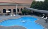 This image shows an outdoor swimming pool area with lounge chairs and a hot tub, situated next to a building with arched openings, all under an overcast sky.