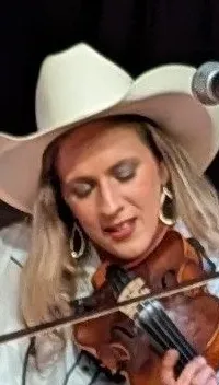 A person in a cowboy hat is performing on a violin on stage in front of a microphone.