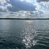 The image shows a serene lake with glistening water reflecting the sunlight, a treelined horizon, and a partly cloudy sky above.