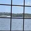 A clear day's view through a window pane with spots and streaks, overlooking a body of water with trees and buildings in the distance.