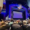 The image shows an elegantly decorated theater with an audience waiting in anticipation for a performance to begin.