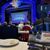 The image shows an audience seated at dining tables inside a theater, waiting for a performance to begin at the 