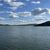 The image shows a tranquil expansive lake with hills in the background under a partly cloudy sky.