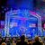 A lively musical performance is underway on a patriotically-themed stage with an audience in the foreground enjoying the show.