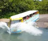 A duck boat filled with passengers is creating a splash as it enters the water from a ramp on a sunny day