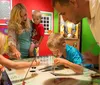 A family is engaged in an interactive exhibit with adults and children focused on an activity at a table