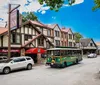 A quaint street scene featuring Tudor-style architecture with a trolley tour bus and vehicles parked alongside the buildings under a clear blue sky