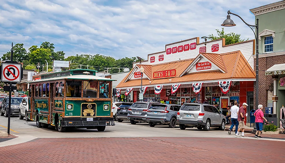 A trolley tour passes through a lively street adorned with American flags in front of quaint shops and parked vehicles under a partly cloudy sky