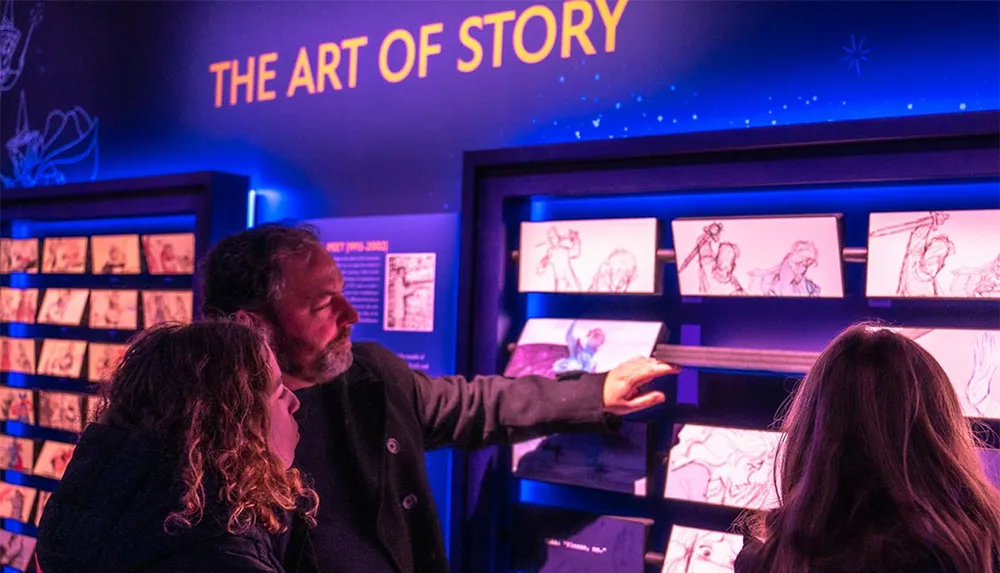 A person is showing something on a screen to two others in an exhibition space dedicated to THE ART OF STORY