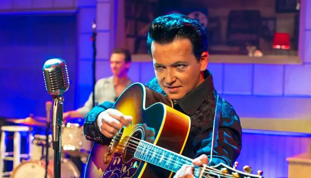 A performer in a vintage-style outfit is playing a guitar and singing into an old-fashioned microphone on stage with a drummer in the background