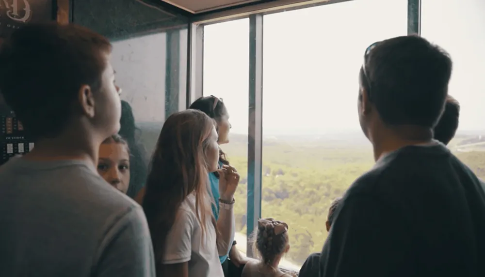 A group of people likely a family are looking out of a large window at a scenic view