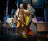 A person in theatrical attire rides a rearing horse puppet on stage set against a backdrop featuring a large full moon