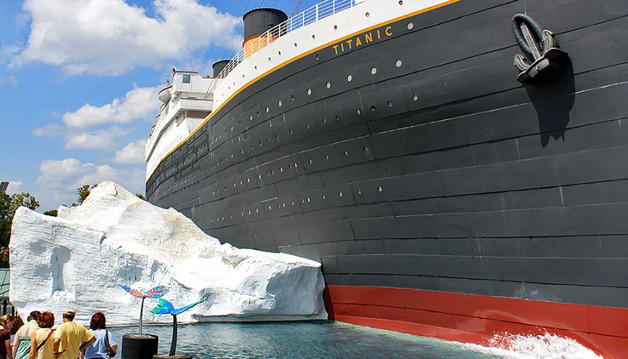 This image features a group of people looking at a large, stationary replica of the Titanic ship next to an artificial iceberg, likely part of a themed attraction or exhibit.