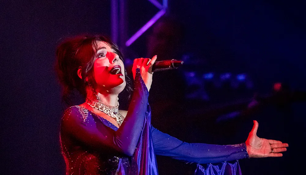 A woman is performing on stage passionately singing into a microphone with dramatic lighting casting shadows on her face