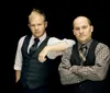 Two men in vests and ties are posing confidently against a black background