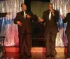 Four smartly dressed men in tuxedos stand together with smiles on their faces set against a golden starburst background with the text PLATTERS Golden Sounds of the 50s in a promotional image