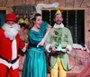 Four people are dressed in colorful and theatrical Christmas-themed costumes expressing exaggerated emotions in what appears to be a festive play or performance