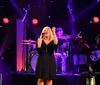 Three singers are performing on stage while a musician accompanies them on a keyboard against a backdrop of a starry curtain and red stage lights