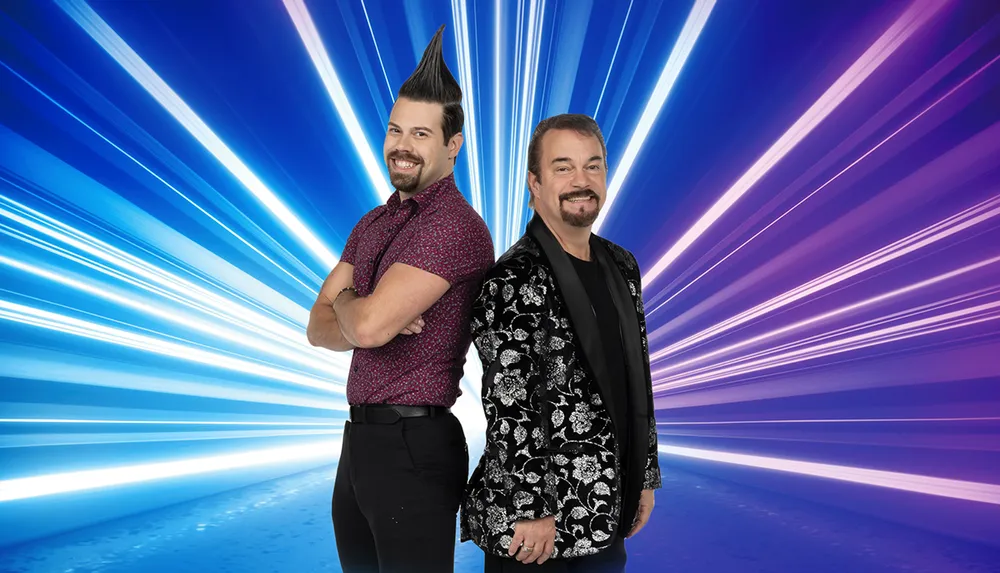 Two smiling men with distinctive hairstyles stand back-to-back against a vibrant blue background with dynamic white light streaks