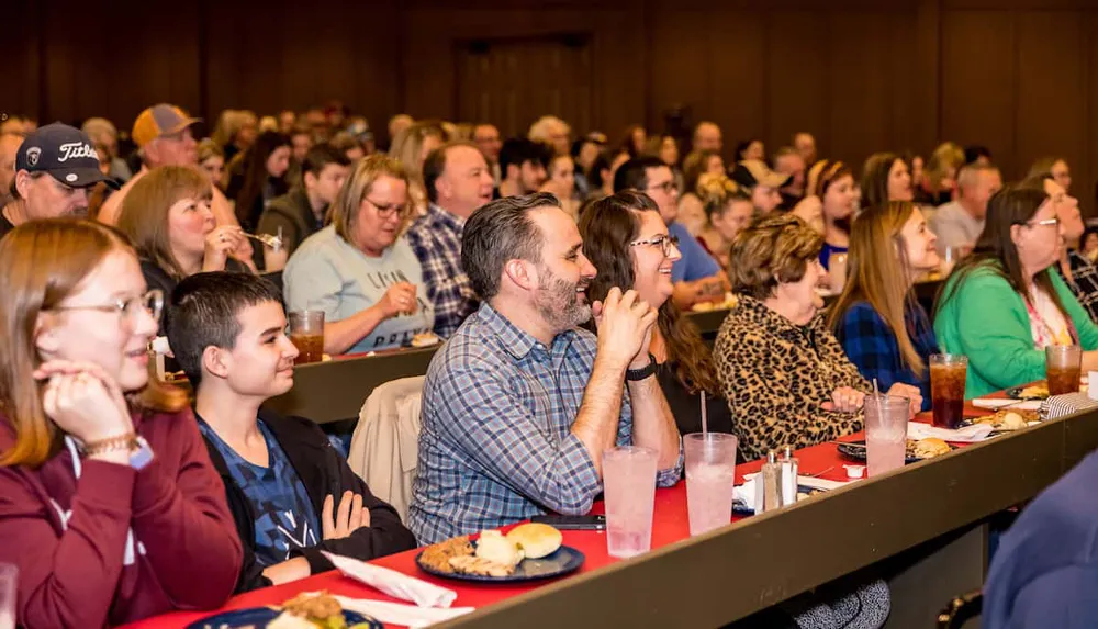 A diverse audience is engaged and attentively watching an event while some enjoy food and beverages