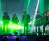 A performer sings passionately on stage flanked by musicians and dancers against a backdrop of warm stage lighting