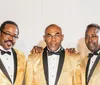 Three men in matching black and orange vests are posing together for a photo with one slightly in front of the other two all looking directly at the camera