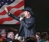 A performer in a cowboy hat is singing into a microphone with an American flag backdrop